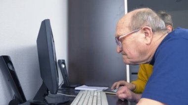 Bilgisayarda çalışan gözlüklü yetmiş yaşında bir adam..