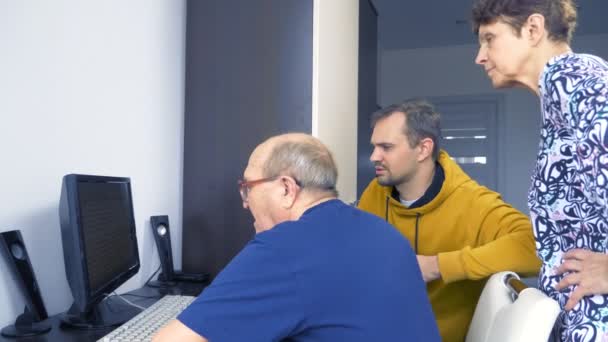 Ein junger Mann erklärt älteren Menschen, wie man einen Computer bedient — Stockvideo