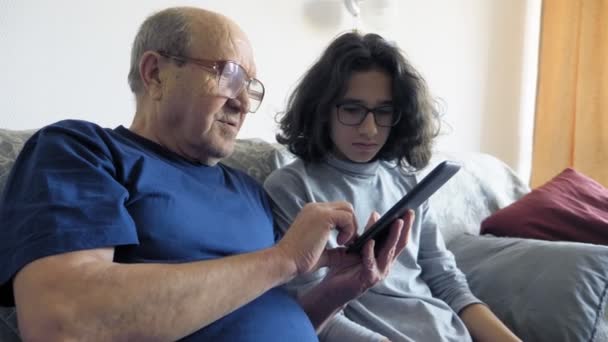 Grandfather and grandson are using an e-book. sitting on the sofa in the room — Stock Video