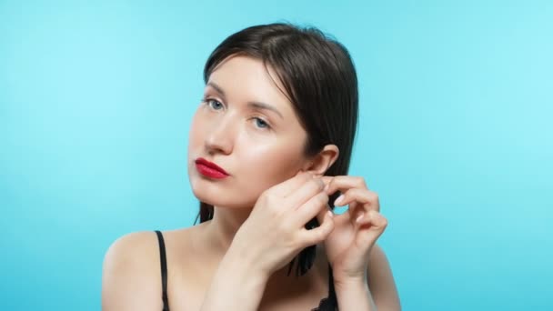 Young beautiful stylish girl wears earrings. blue background — Stok video