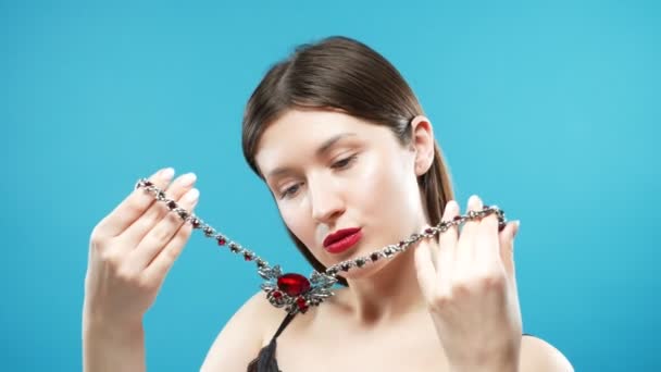 La jeune fille essaie sur un collier massif magnifique avec des pierres rouges. fond bleu — Video