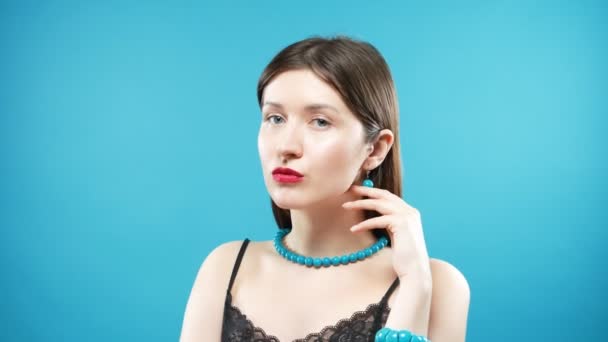 Young beautiful girl in the bracelet and the beads of turquoise. blue background. — Stock Video