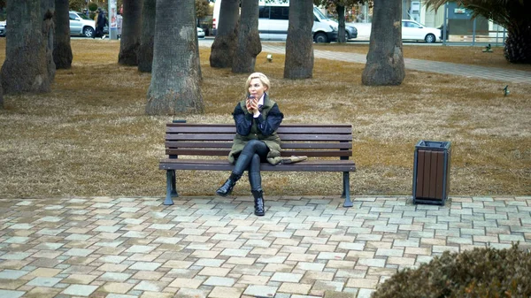 Mujer rubia elegante sentada en el banco en otoño Park —  Fotos de Stock