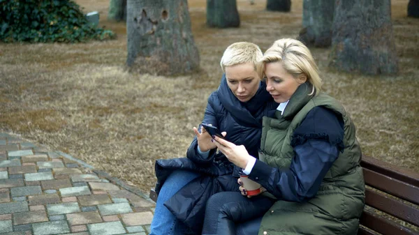 Две взрослые блондинки разговаривают, сидя на скамейке в парке . — стоковое фото