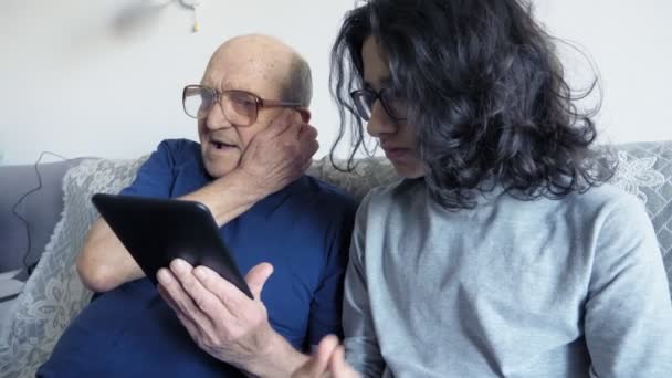 Dziadek i wnuk używają e-booka. siedząc na kanapie w pokoju — Wideo stockowe