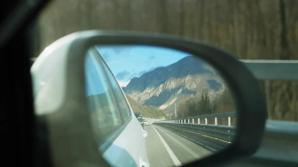 snowy mountains reflected in the rearview mirror while the vehicle is in motion