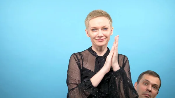 Humorvolles Konzept. Frau applaudiert einem Mann, der ihretwegen hervorlugt. blauer Hintergrund — Stockfoto