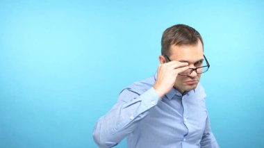  handsome guy takes off his glasses, looks at the camera. blue background.