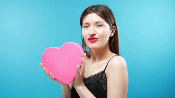 Beautiful young girl holding a box in the shape of a heart. blue background — Stock Photo, Image