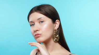 young beautiful stylish girl wears earrings. blue background