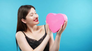 beautiful young girl holding a box in the shape of a heart. blue background
