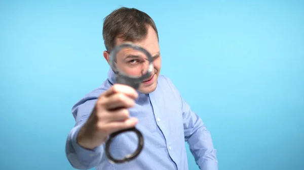 Een man kijkt in de camera en toont de handboeien. blauwe achtergrond — Stockfoto