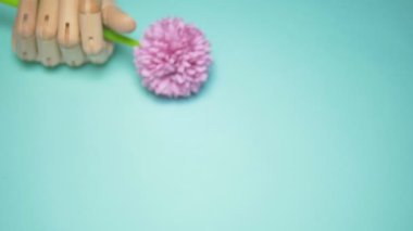 wooden hand holding artificial flowers. blue background