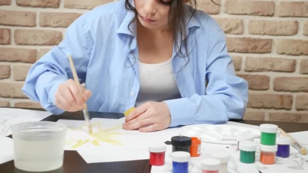 Hermosa joven dibuja pinturas en el estudio. contra una pared de ladrillo — Vídeos de Stock