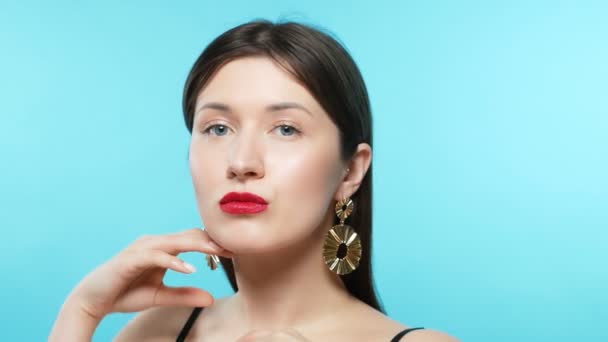 Young beautiful stylish girl wears earrings. blue background — Stok video