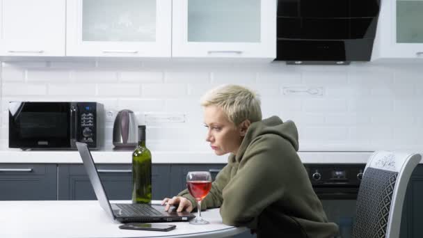 Hermosa mujer con estilo está utilizando el ordenador portátil y beber vino, en la cocina — Vídeos de Stock