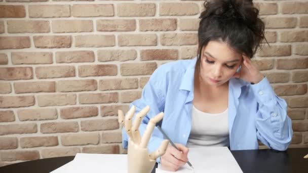 Mooi meisje, de kunstenaar maakt een schets van een kunstmatige houten hand. — Stockvideo