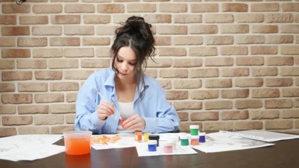 Hermosa joven dibuja pinturas en el estudio. contra una pared de ladrillo — Vídeo de stock