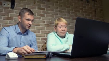 Yaşlı kadın ve genç adam dizüstü bilgisayarlarını tuğla duvara karşı kullanıyorlar.