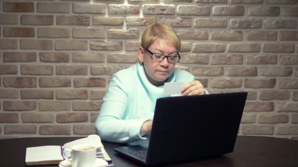 Een oudere vrouw gebruikt thuis een laptop en creditcard — Stockvideo