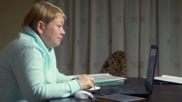 Літня жінка говорить на відео, сидячи перед ноутбуком — стокове відео