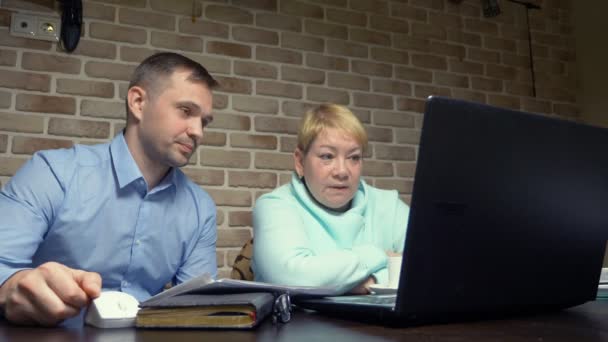 Older woman and young man using laptop together against a brick wall — Stock Video