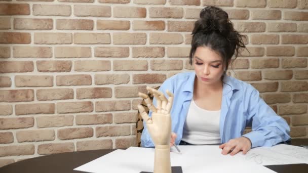 Artista ragazza disegna uno schizzo a matita da una figura di legno di un uomo — Video Stock