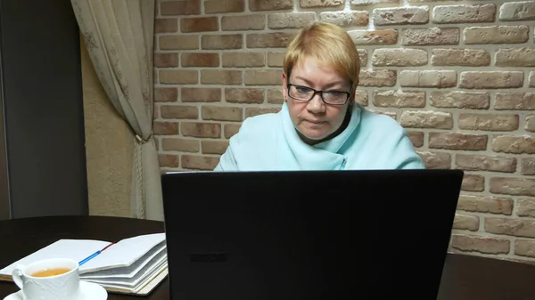 En äldre kvinna arbetar med en laptop, sitter vid ett bord. Äldre arbetssätt — Stockfoto