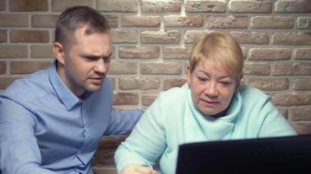 老年妇女和年轻男子靠着砖墙一起使用笔记本电脑 — 图库视频影像