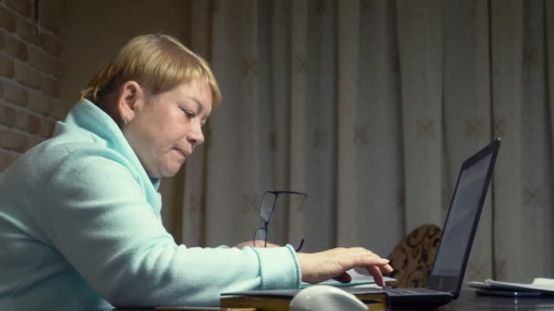 Anciana hablando en el video cuando se sienta delante de la computadora portátil — Vídeo de stock