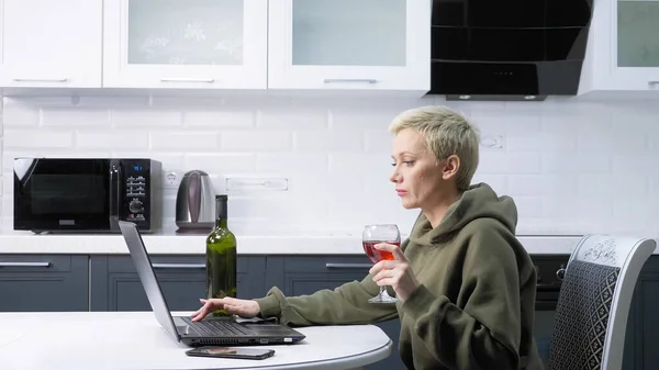 Hermosa mujer con estilo está utilizando el ordenador portátil y beber vino, en la cocina — Foto de Stock