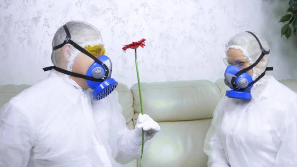 People in protective suits and respirators. a man gives a woman a flower — Stock Photo, Image