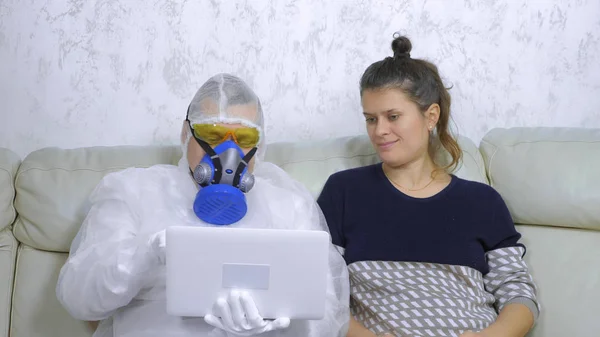 A man in a protective suit uses a laptop next to a woman in casual clothes — Stock Photo, Image