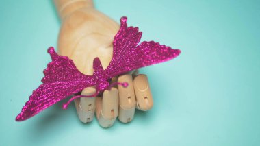 wooden hand holding an artificial butterfly . blue background