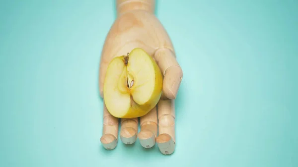 Main en bois tenant la moitié d'une pomme verte, fond bleu — Photo