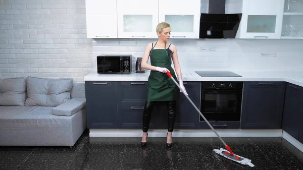 Mujer con estilo en un corsé de cuero y delantal lava el suelo de la cocina. humor — Foto de Stock