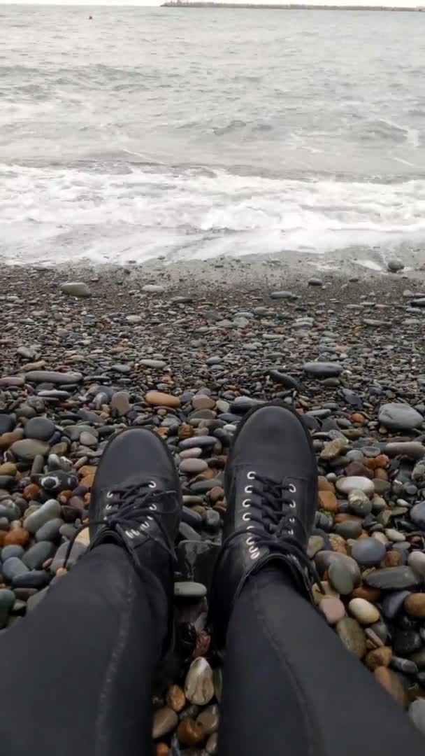 Frauenbeine in schwarzen Schuhen auf dem Hintergrund des Meeres. Kieselstrand. — Stockvideo