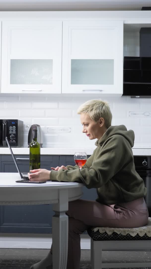 Vertikální výstřel. stylová žena používá notebook a pije víno v kuchyni — Stock video
