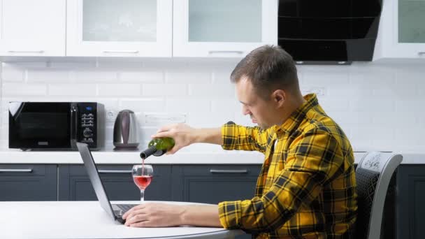 Um homem de camisa xadrez usa um laptop bebendo vinho na mesa da cozinha — Vídeo de Stock