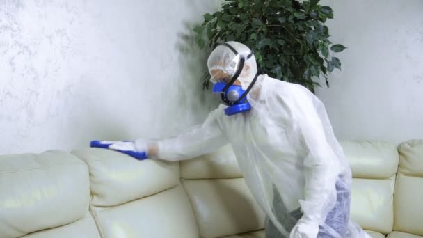 Frau in Schutzanzug und Atemschutzmaske wischt Ledersofa im Zimmer. — Stockvideo