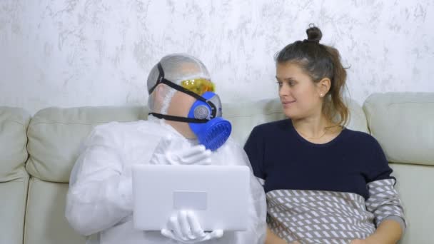Un hombre con un traje de protección utiliza un ordenador portátil junto a una mujer en ropa casual — Vídeo de stock