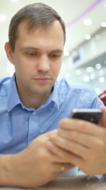 Dikey çekim. Adam bir kafede otururken akıllı telefon kullanınca şaşırıyor.
