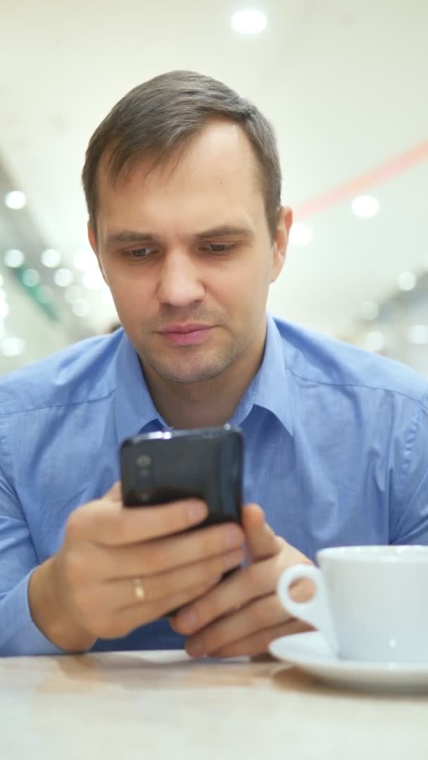 Dikey çekim. Adam bir kafede otururken akıllı telefon kullanınca şaşırıyor. — Stok video