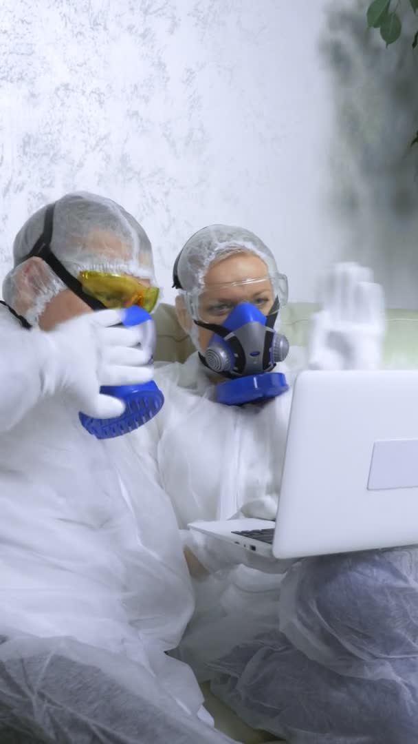 Vertikal erschossen Menschen in Schutzanzügen und Atemschutzmasken zu Hause mit einem Laptop — Stockvideo