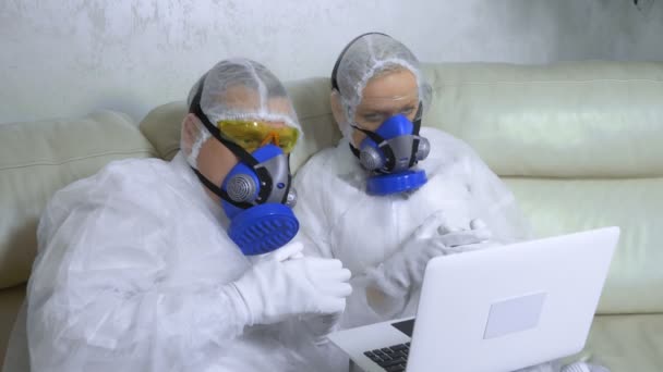 Mensen in beschermende pakken en ademhalingstoestellen thuis met een laptop — Stockvideo