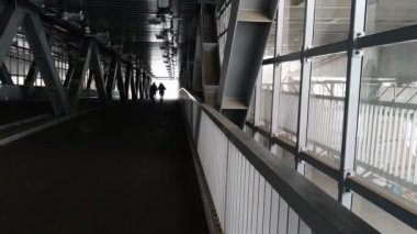 Kışlık ceketli yalnız bir adam metal bir yaya geçidinden geçiyor..