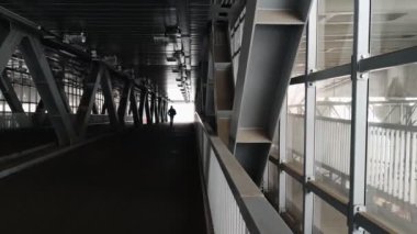 Kışlık ceketli yalnız bir adam metal bir yaya geçidinden geçiyor..