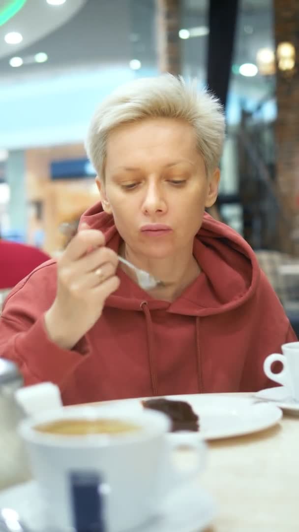 Vertikalt skott. trött kvinna äter chokladkaka på ett café och dricker kaffe — Stockvideo