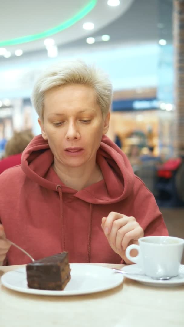 Κάθετη βολή. κουρασμένη γυναίκα τρώει κέικ σοκολάτας σε ένα καφέ και πίνει καφέ — Αρχείο Βίντεο