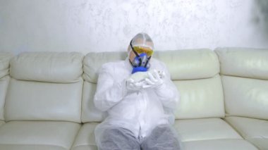 Koruyucu giysili ve solunum cihazlı bir adam beyaz bir fareye bakıyor.